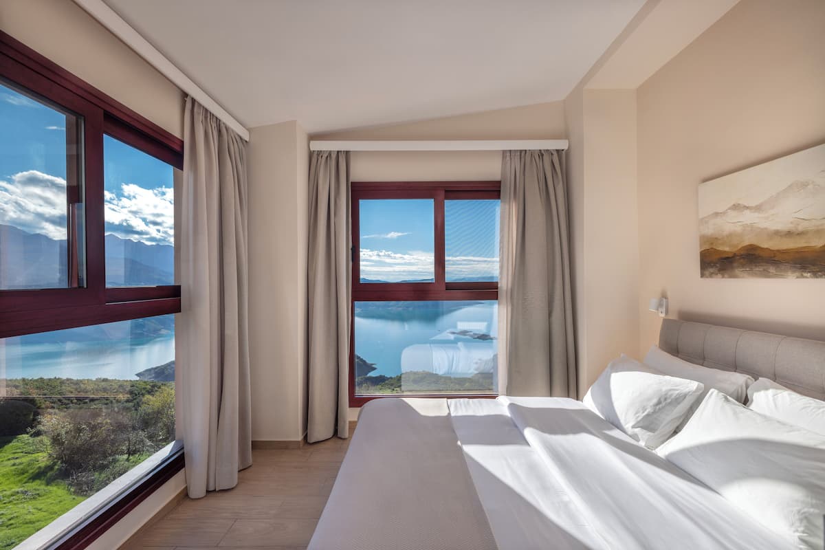 Een hotelkamer met een groot raam dat uitzicht biedt op bergen en een meer.