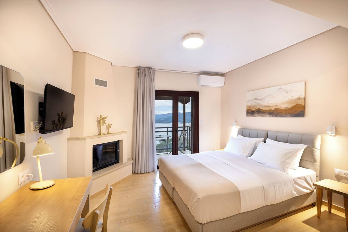 Een moderne hotelkamer met een groot bed, een flatscreen televisie, een bureau met een lamp, een open haard en een balkon met uitzicht.