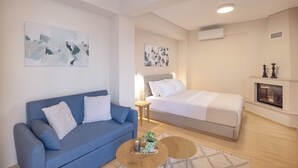 A modern bedroom with a bed, a blue sofa, a small table, and artwork on the walls. - Lake Kremasta Hotel (Agrafa)