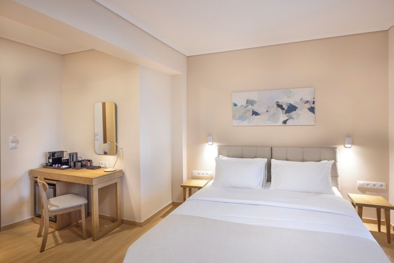 Una camera d'albergo con un letto, una scrivania, una sedia, uno specchio e un quadro appeso al muro.