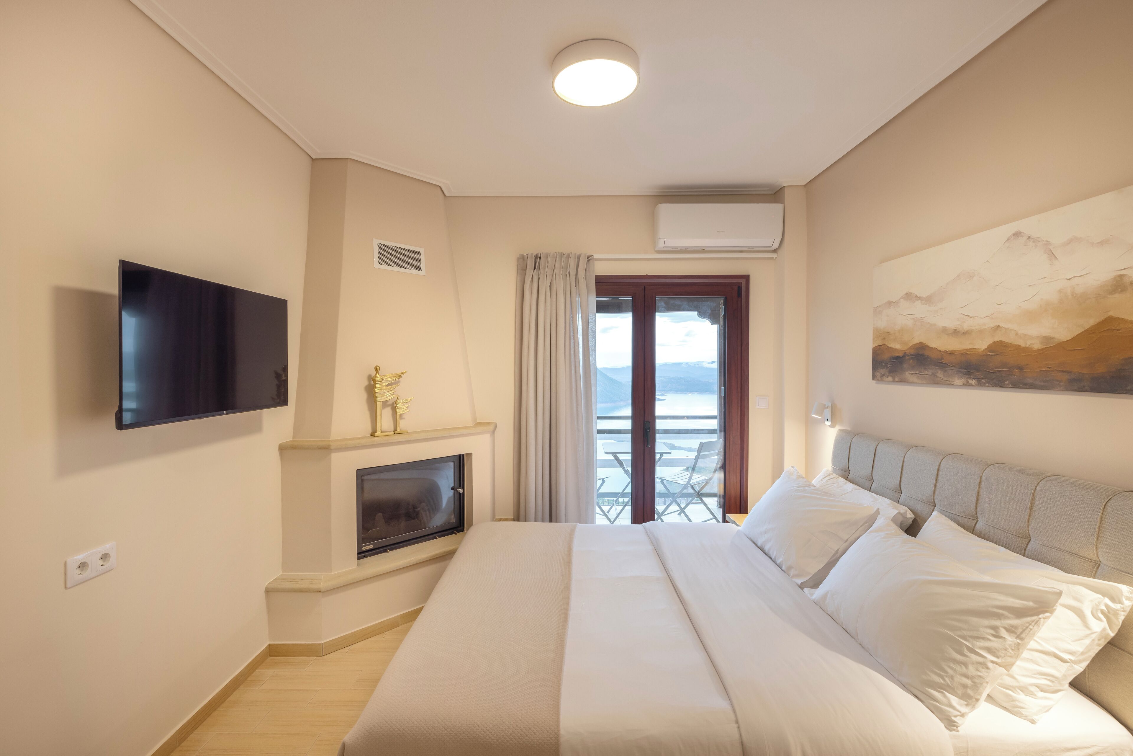 A hotel room with a bed, a flat-screen TV, a fireplace, and a balcony with a view.