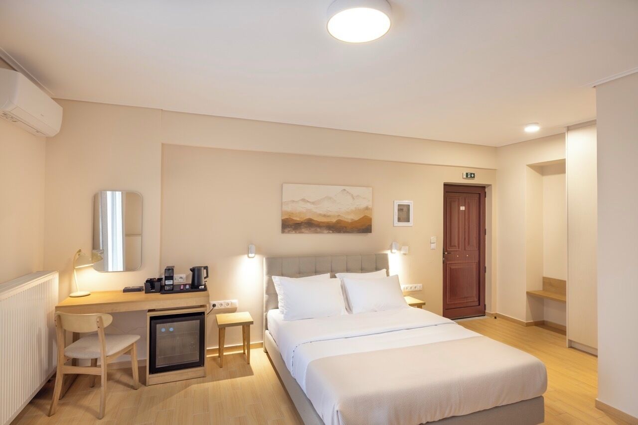 Une chambre d’hôtel équipée d’un lit, d’un bureau avec un ordinateur, d’une chaise, d’un petit réfrigérateur et d’une porte signalée comme issue de secours.