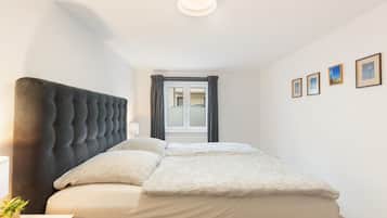 Ein Schlafzimmer mit einem großen Bett, einem Kopfteil, einem Nachttisch, einer Lampe und einem Fenster mit Vorhängen.