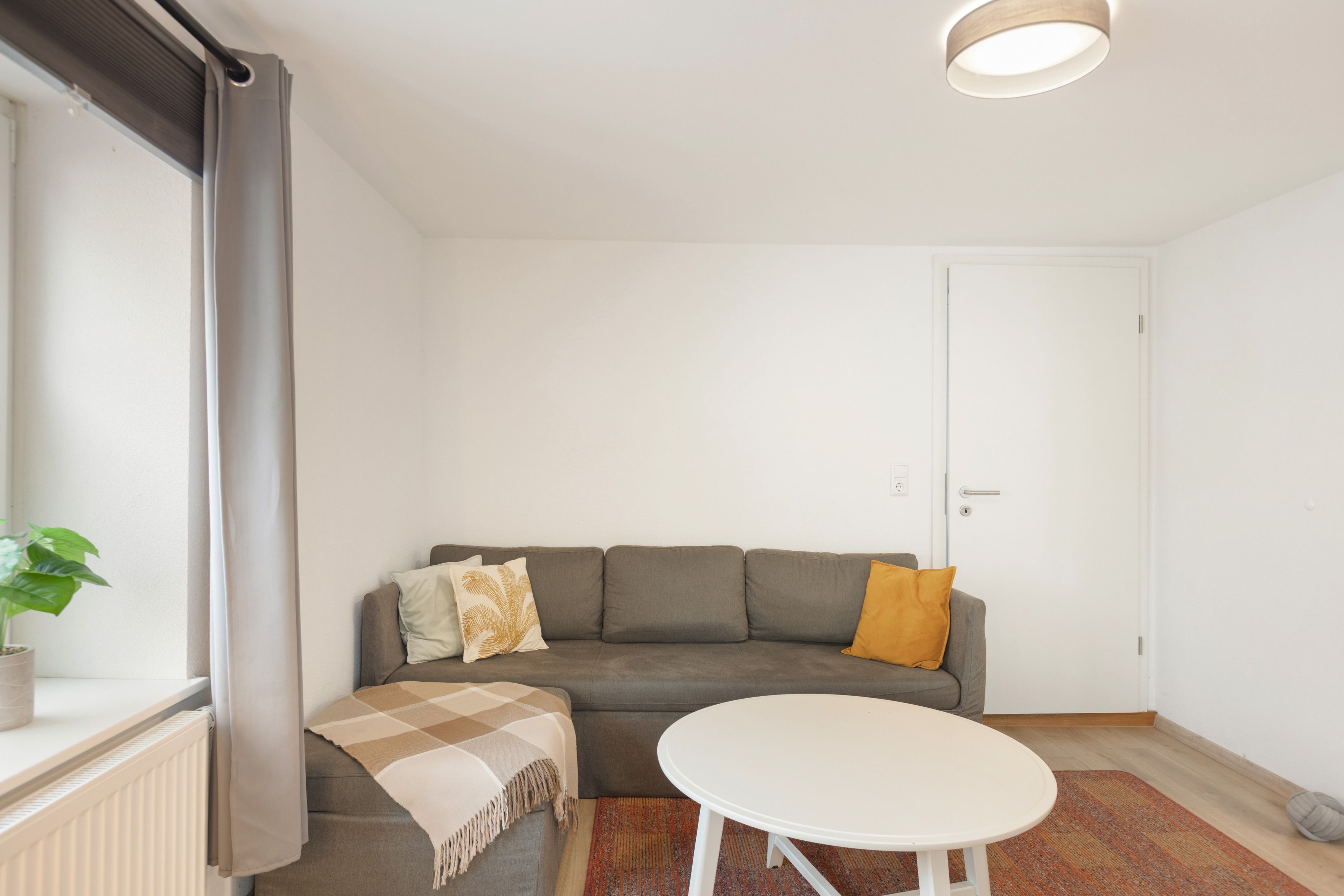Ein modernes Wohnzimmer mit einem grauen Sofa, einem weißen Tisch und einer Topfpflanze.