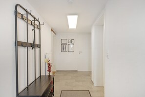 Un pasillo con un perchero, un radiador, un florero con flores y cuadros en la pared.
