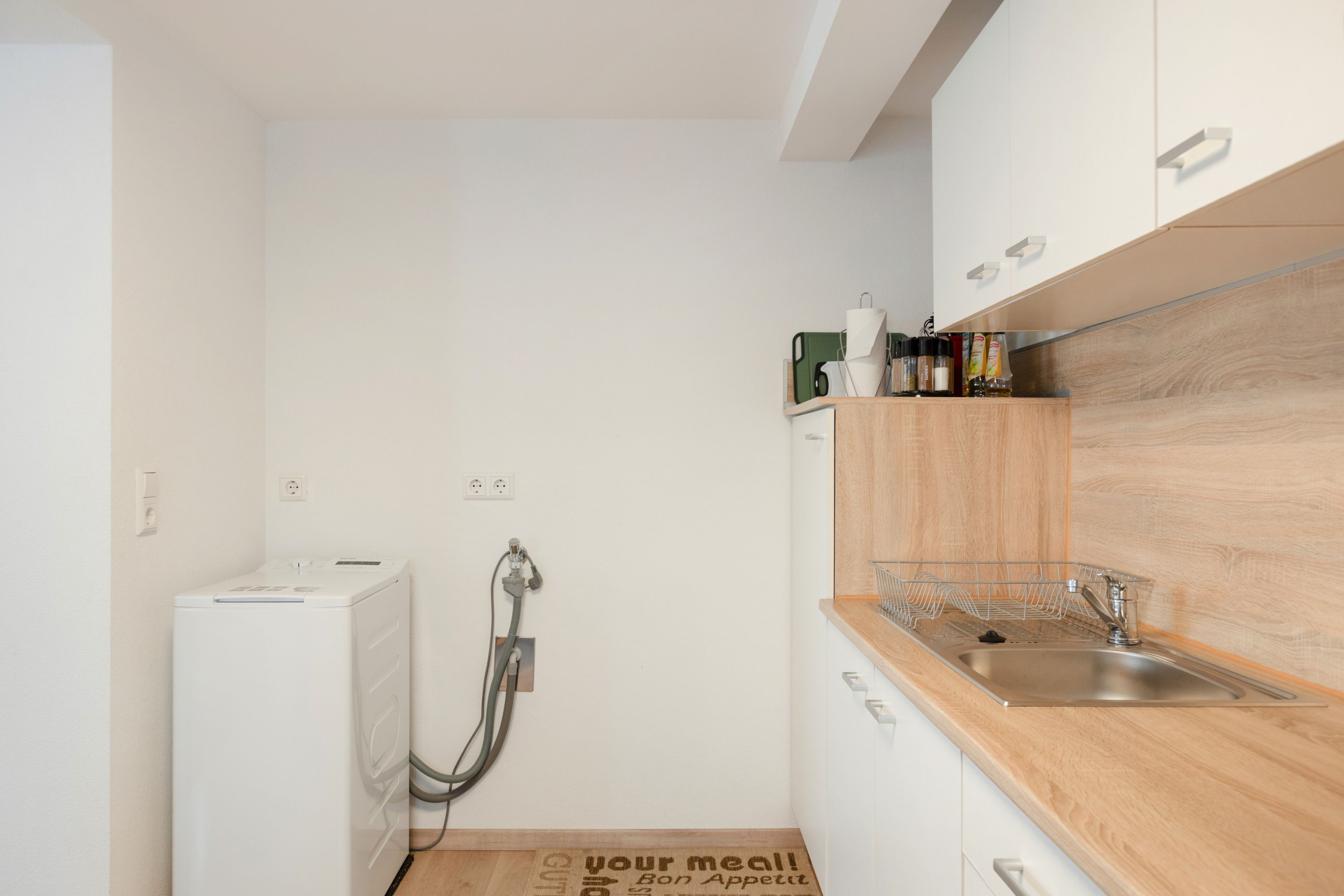 Eine kleine Küche mit integriertem Geschirrspüler, einer Holz Arbeitsplatte und einem Edelstahl-Spülbecken.