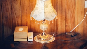 A wooden nightstand with a lamp, a box, and a small electronic device. - Havenora Retreat (Tay Hoa Lu)