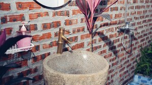 A bathroom with a stone sink, a brass faucet, and a shower head against a brick wall. - Havenora Retreat (Tay Hoa Lu)