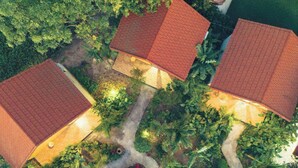 An aerial view of a residential area with three houses, each with a red-tiled roof, surrounded by lush greenery and a well-maintained garden. - Havenora Retreat (Tay Hoa Lu)
