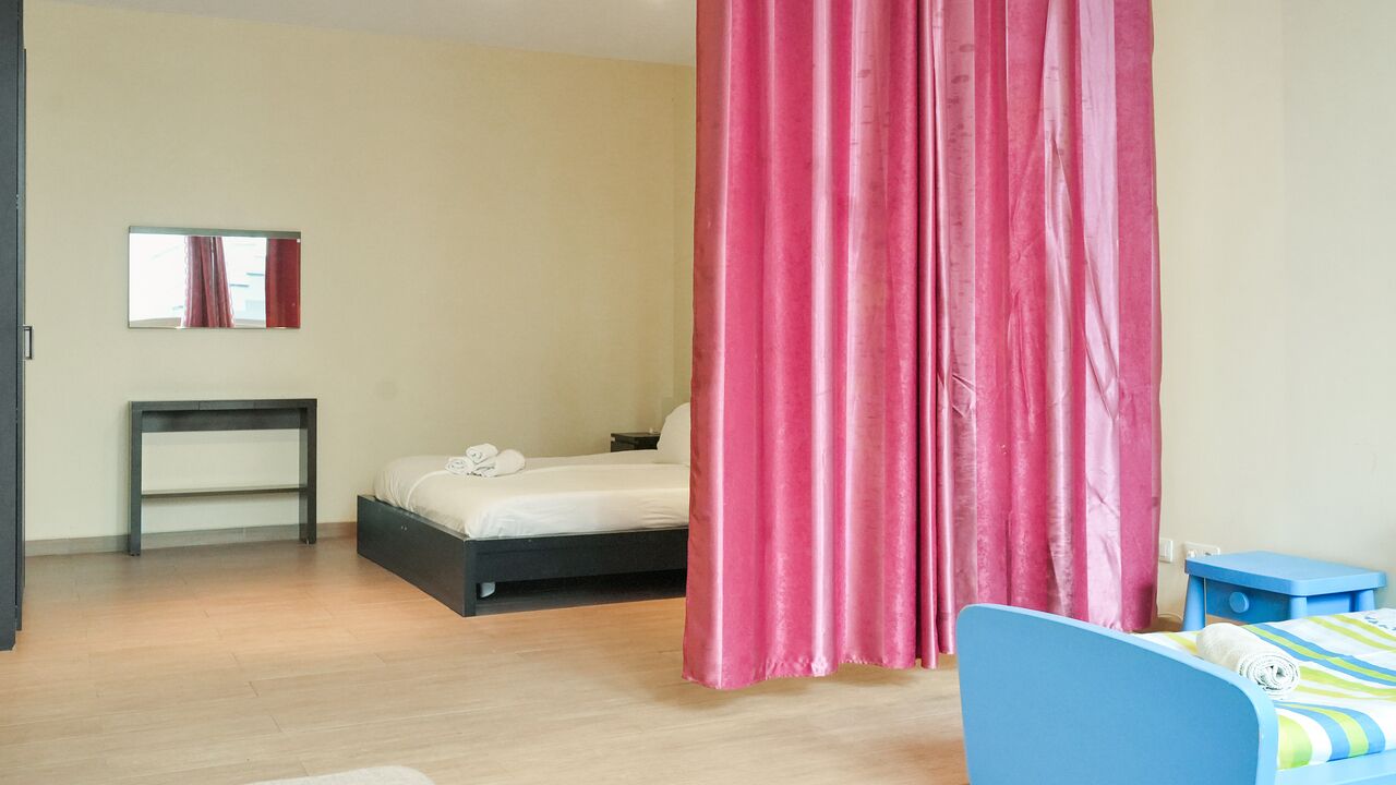 A bedroom with a bed, a bedside table, a mirror, and a window with curtains.
