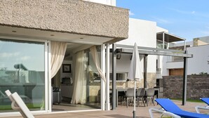 A modern outdoor patio with glass doors, a dining area, and blue lounge chairs. - Private Villa with Pool - Close to the Beach (Costa Adeje)