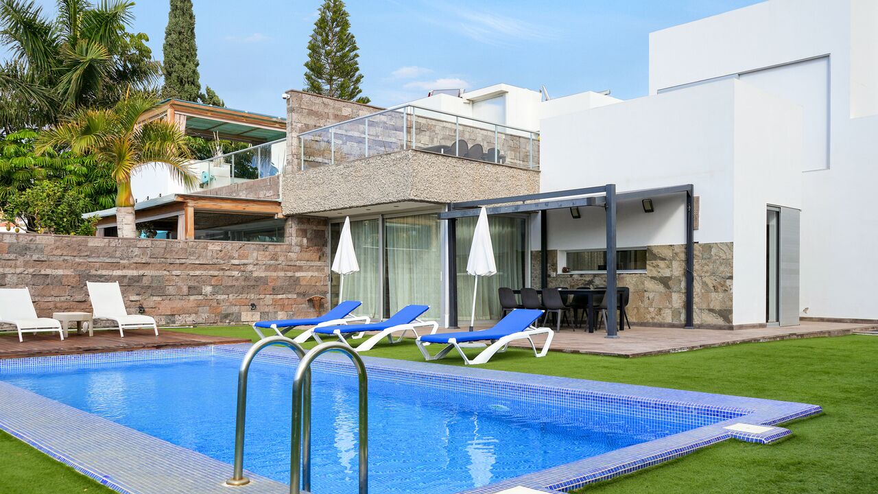 A modern pool area with a clear blue pool, lounge chairs, and a covered patio.