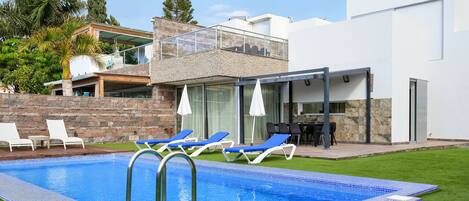 A modern pool area with a clear blue pool, lounge chairs, and a covered patio.