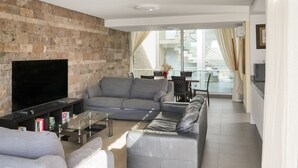 A modern living room with a stone wall, grey sofas, a flat-screen TV, and a glass coffee table. - Private Villa with Pool - Close to the Beach (Costa Adeje)