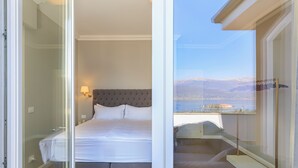 A bedroom with a bed, a nightstand, a lamp, and a view of a mountain and lake. - Lake 270 Apartment (stresa)