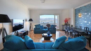 A living room with a large flat-screen TV, a sofa, a coffee table, and a dining area with chairs and a table. - Lake 270 Apartment (stresa)