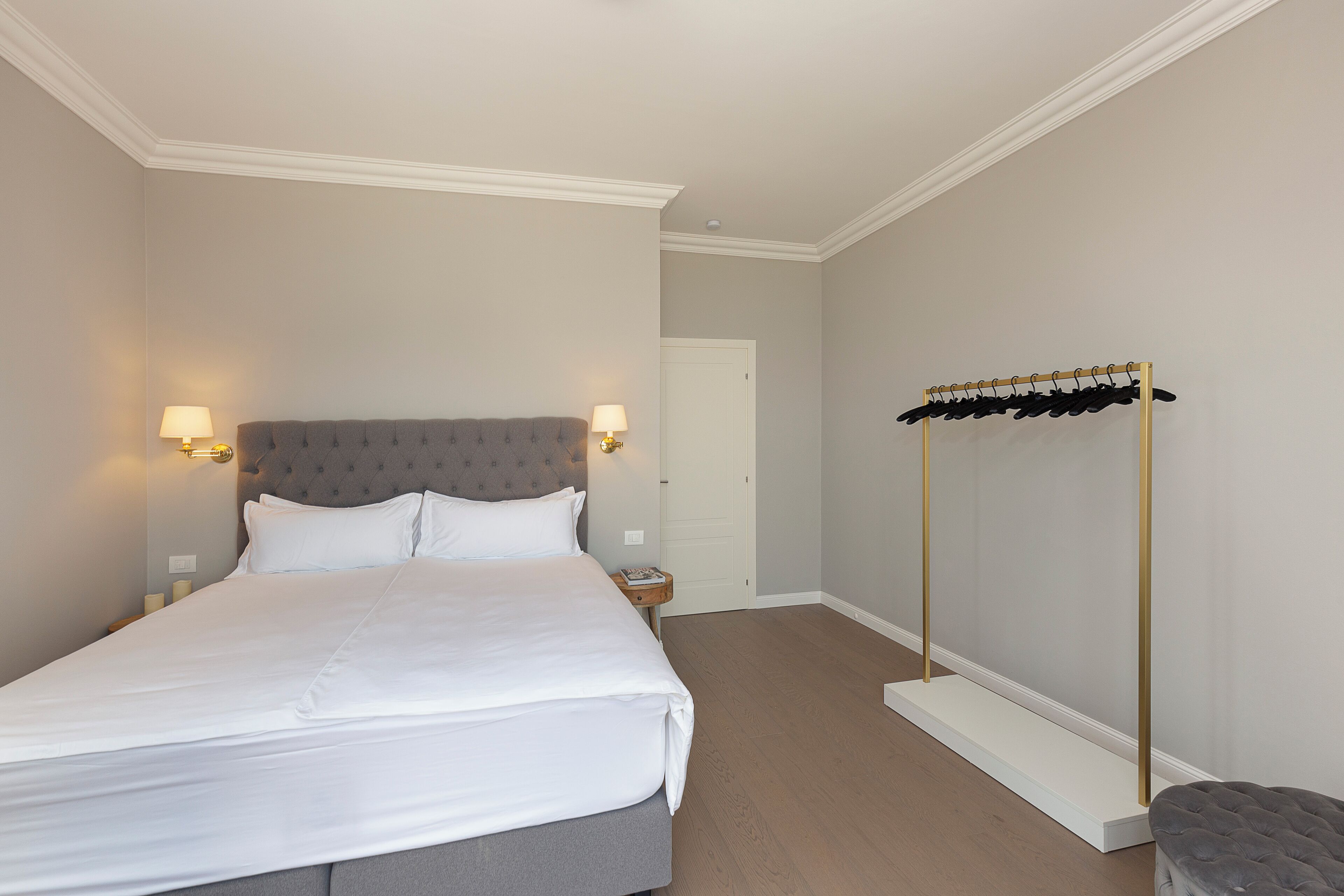 Ein ordentlich eingerichtetes Schlafzimmer mit einem großen Bett, Nachttischlampen, einem Kleiderschrank und einem kleinen Hocker.