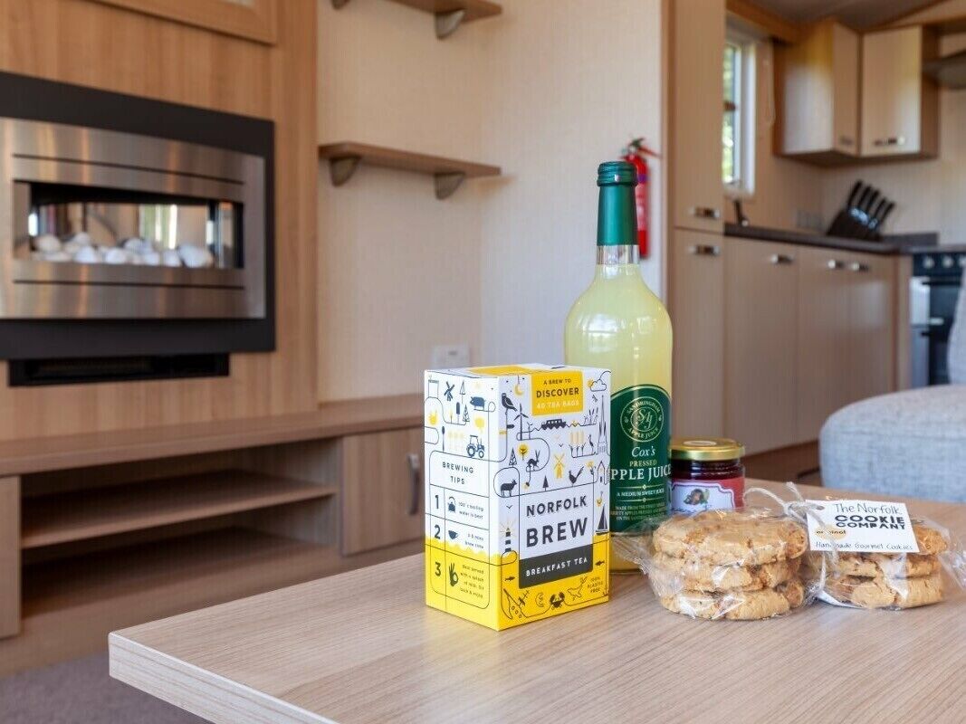 A kitchen with a wooden countertop, a box of Norfolk Brew breakfast tea, a bottle of apple juice, and packaged cookies.