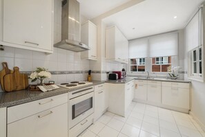 A modern kitchen with white cabinets, a stainless steel range hood, and a granite countertop. - Upscale Central London Apartment (London)