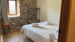 Une chambre avec un mur en pierre, un lit en bois, un luminaire suspendu et une fenêtre donnant sur un beau paysage.