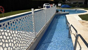 A swimming pool with a white lattice fence, clear blue water, and a tiled deck area. - CasaMar Playa (Estepona)