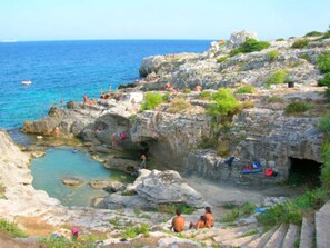 A rocky coastal area with people relaxing on the cliffs and in the water. - La Casetta Di Novaglie - Puntaverde Con Vista Mare (Alessano)