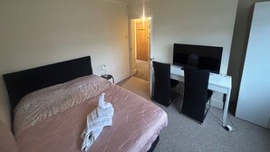 Ein Hotelzimmer mit Bett, Schreibtisch, Fernseher und einer Tür zu einem Badezimmer.