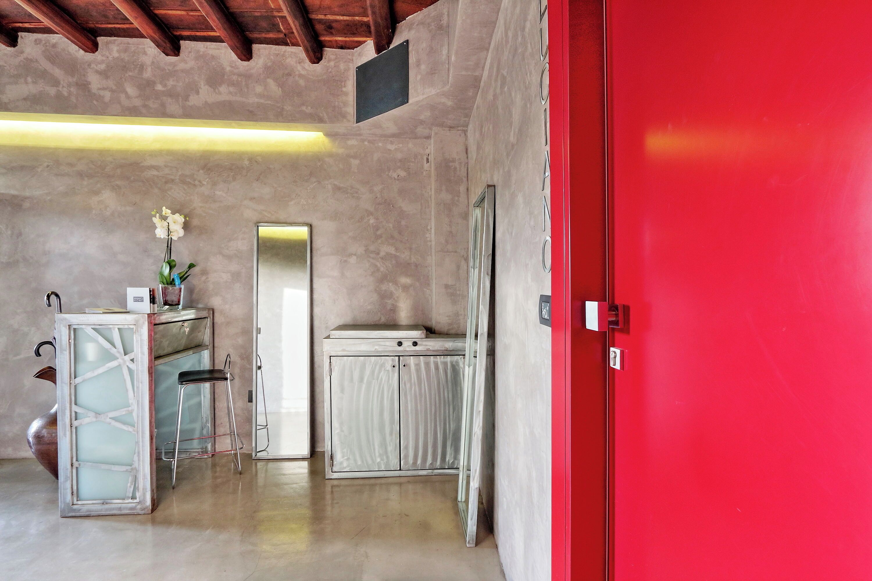 A room with a red door, a white cabinet, a stool, and a mirror.