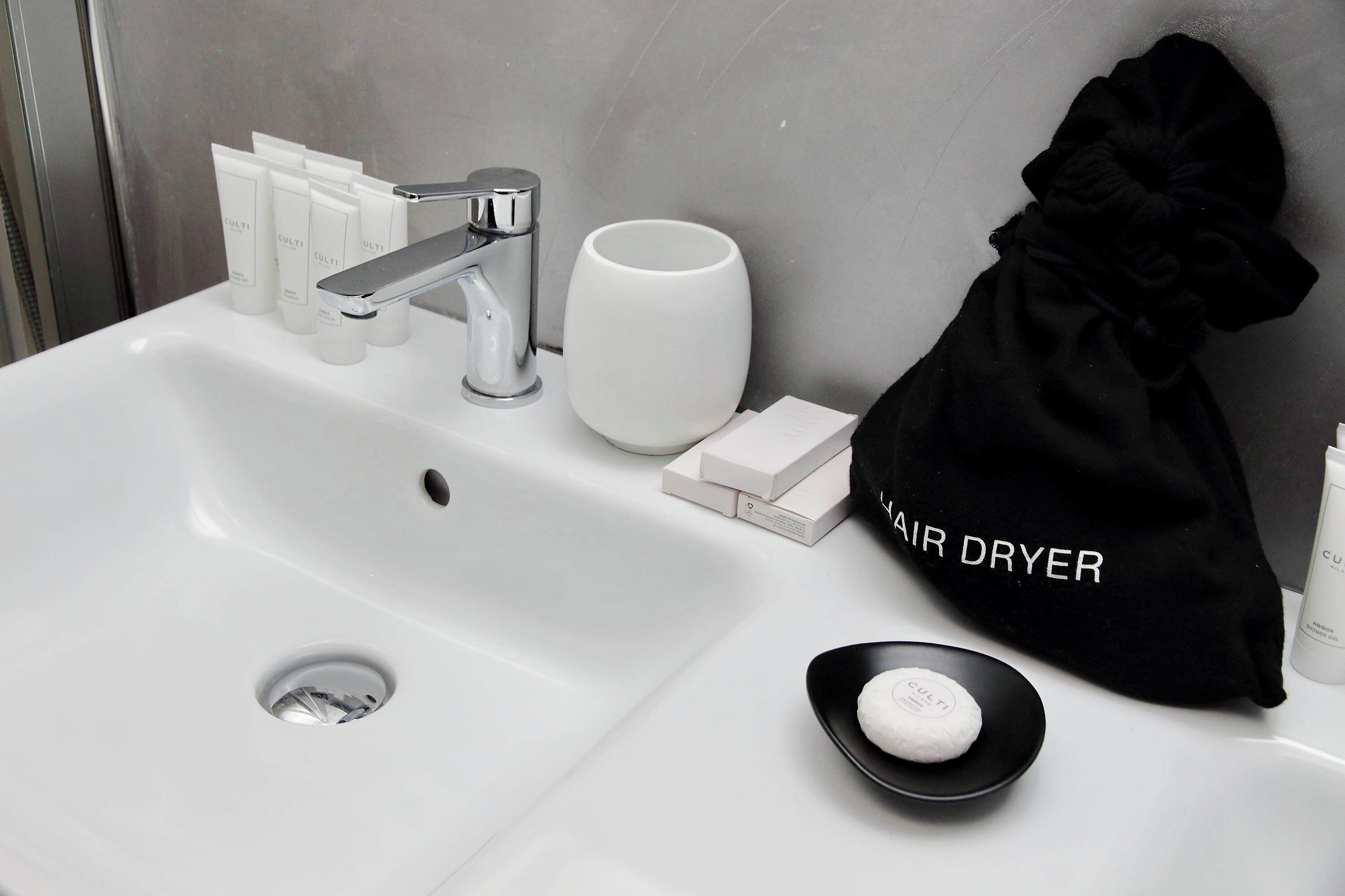 Un lavandino in bagno con articoli da toilette, un sacchetto per asciugacapelli e una tazza.