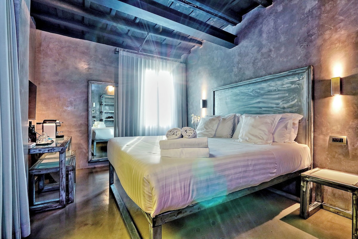 Un dormitorio moderno con una cama grande, una mesita de noche, un espejo y una ventana con cortinas.
