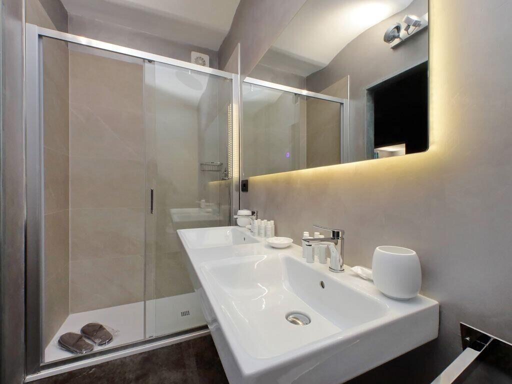 A modern bathroom with a glass shower enclosure, a large white sink, and a mirror with integrated lighting.