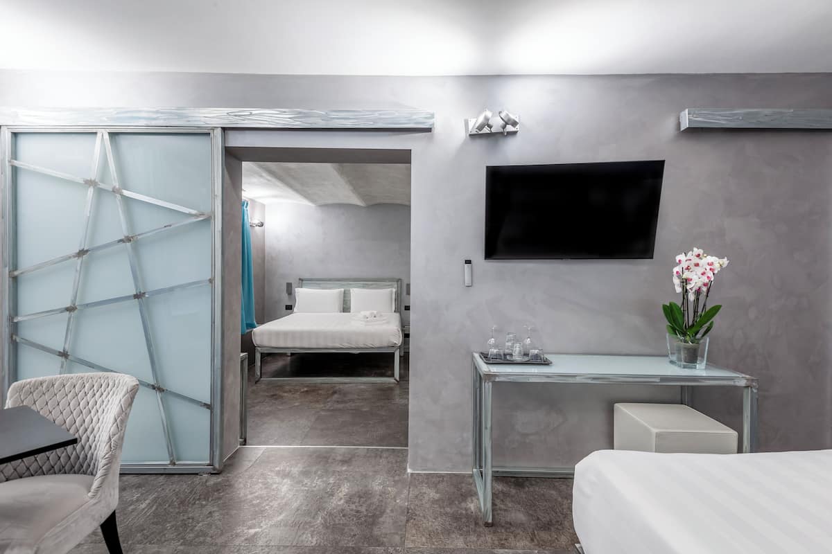 Habitación de hotel moderna con cama, escritorio de cristal, televisor y puerta corredera.