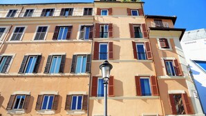 Un edificio de varios pisos con fachada color beige, múltiples ventanas con contraventanas marrones y un farol en primer plano.