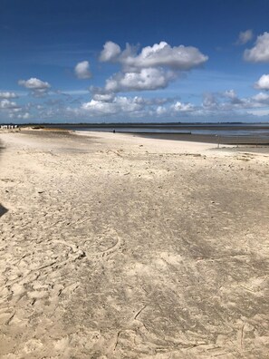 A sandy beach with footprints and a metal railing.