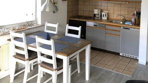 A modern kitchen with grey cabinets, a wooden dining table, and white chairs. - Apartment 'Wilde' with Wi-Fi (Hooksiel)