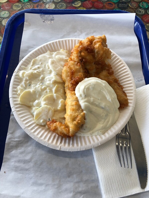 A plate with a breaded item, a creamy sauce, and a white sauce, on a paper plate with a fork and knife beside it.