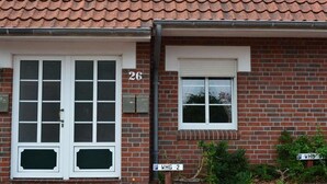 A two-story brick building with a red-tiled roof, a white-framed double door, and a small window with a shutter. - Apartment 'Wilde' with Wi-Fi (Hooksiel)
