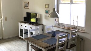 A dining area with a table, chairs, a television, and a window with curtains. - Apartment 'Wilde' with Wi-Fi (Hooksiel)