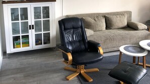 A living room with a black leather chair, a white cabinet with glass doors, a grey sofa, and a painting of a lighthouse. - Apartment 'Wilde' with Wi-Fi (Hooksiel)