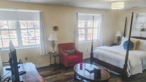Une pièce avec un lit, un fauteuil rouge, une petite table, un téléviseur et une fenêtre.