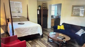 Une chambre d’hôtel avec un lit à baldaquin, un canapé, un fauteuil rouge, une table basse et une vue sur la cuisine et l’extérieur.
