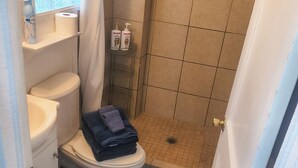 Une petite salle de bain comprenant des toilettes, un espace douche et une petite étagère où sont rangés les articles de toilette.