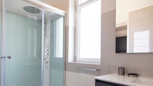 A modern bathroom with a glass shower enclosure, a large window, and a dark-toned vanity. - Color Dream Residence- Intimate Suite Pink (Capitolo)