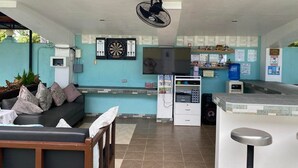 Un hall d’hôtel moderne avec un canapé, un téléviseur, un jeu de fléchettes et un comptoir d’accueil.