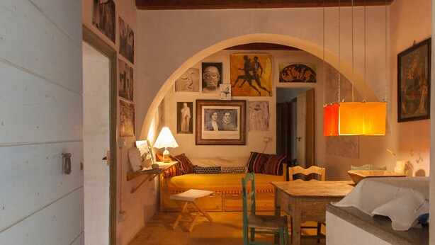 Une pièce confortable avec un lit, un bureau et une chaise. Des tableaux encadrés ornent le mur et une lampe se trouve sur le bureau.