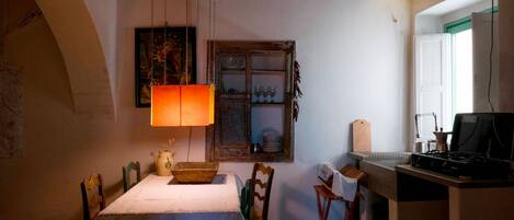 A cozy dining area with a table set for two, a hanging lamp, and a rustic window with shelves above.