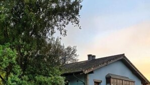 A two-story building with a light blue facade, stone foundation, and a well-maintained garden with trimmed hedges and a paved walkway. - la casona encanto rural (Llanes)