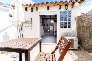 A patio with a wooden table and chairs, a white umbrella, and a wall-mounted drying rack. - Studio for couples with terrace on the beach (València)