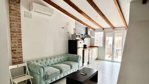 A modern living room with a light green sofa, a black coffee table, and a kitchen area with a refrigerator and stove. - Studio for couples with terrace on the beach (València)