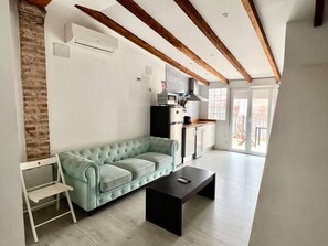 A modern living room with a light green sofa, a black coffee table, and a kitchen area with a refrigerator and stove. - Studio for couples with terrace on the beach (València)